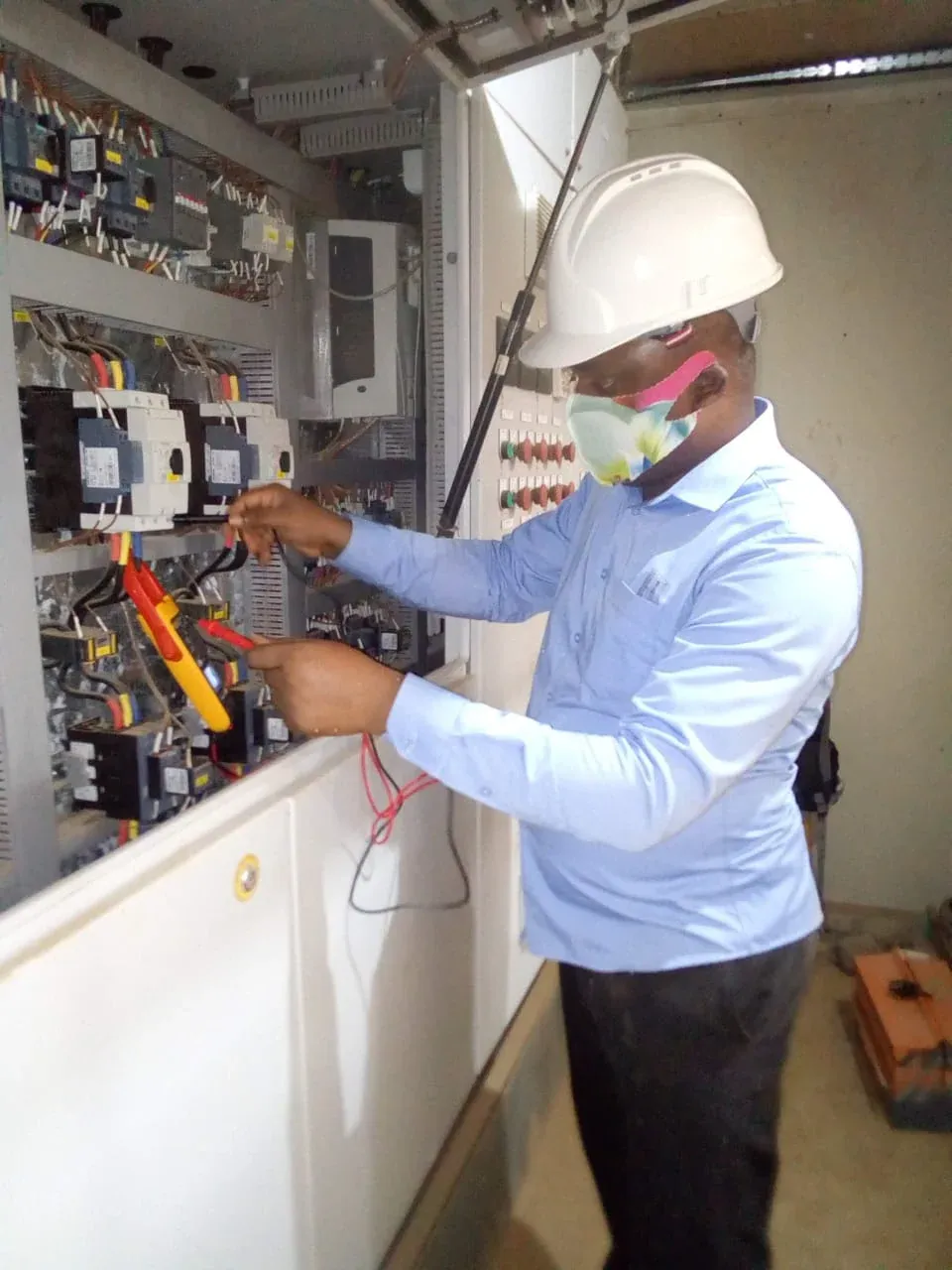 Engineer testing contactor wiring inside a distribution panel with a clamp meter