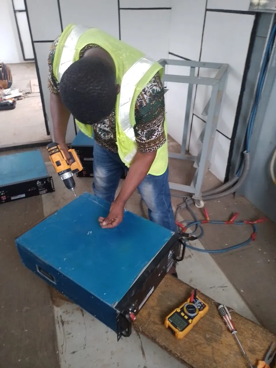 Technician drilling mounting points on a steel equipment enclosure